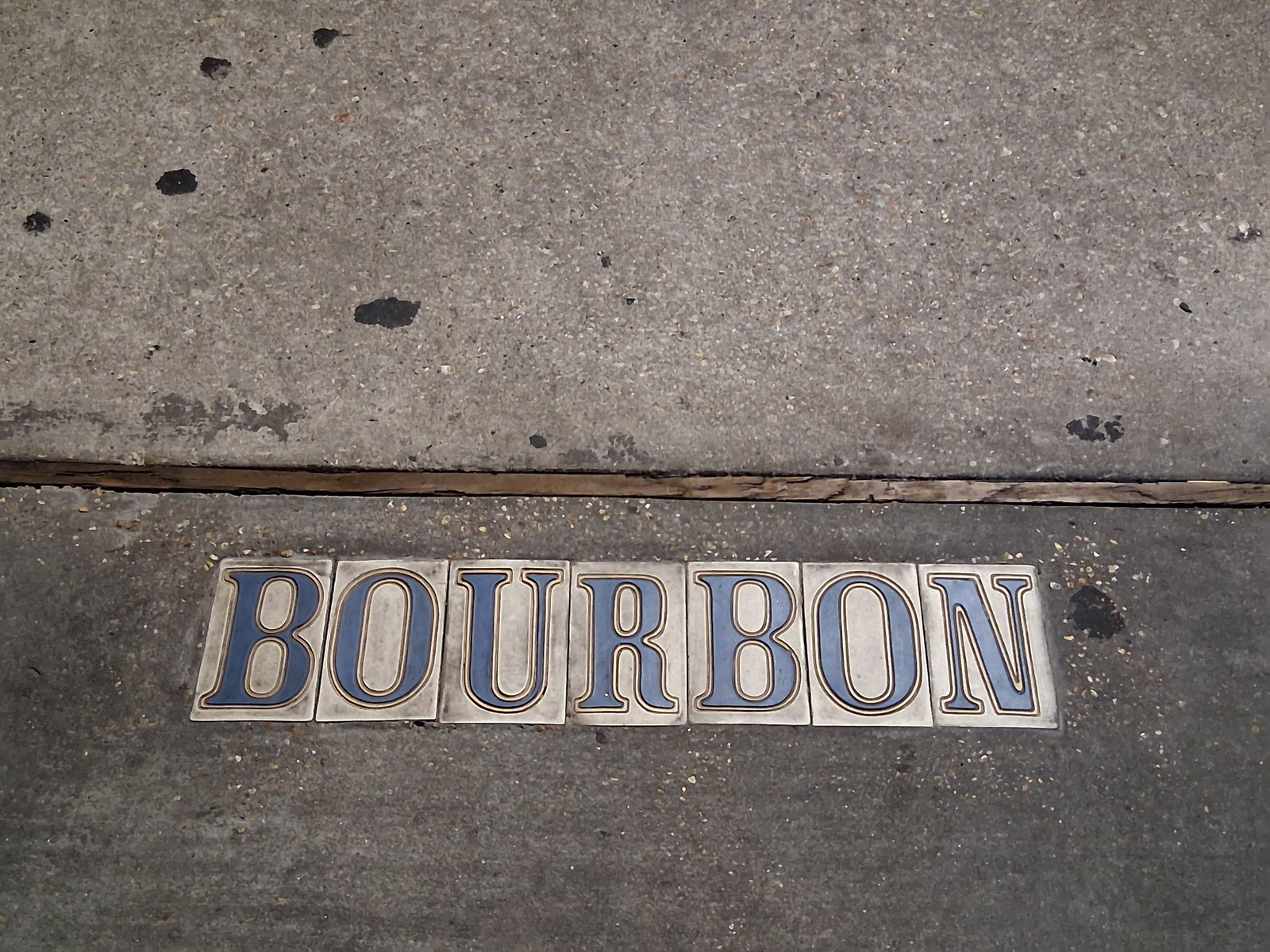 The Bourbon Street tile marker set into a French Quarter sidewalk. The visitor economy runs on the street the marker names.